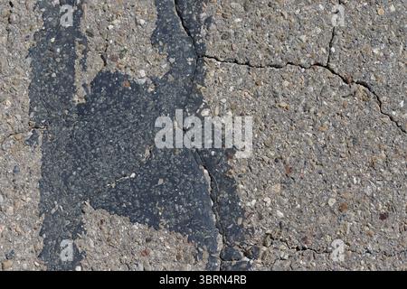 Close-up of damaged asphalt surface with patching and cracks. Texture visible, light grey and dark grey tones dominate. Stock Photo