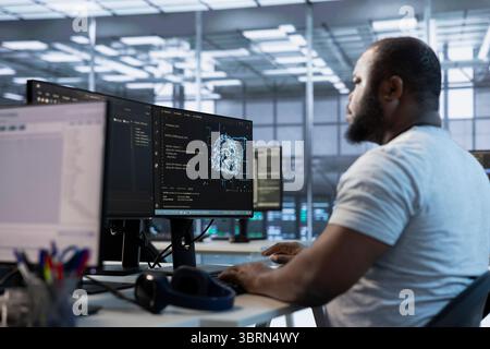 Admin working in server hub, sitting at computer desk, checking recovery plan, monitoring data center energy consumption across components, making sure sensors are functioning optimally Stock Photo