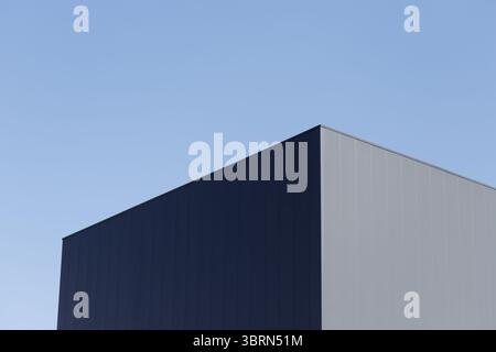 A building's corner is shown against a clear sky, with one side dark blue and the other light gray, both with vertical paneling. Stock Photo