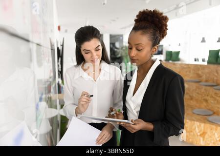Two multiracial businesswomen making data review using digital tablet Stock Photo