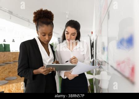 Two attractive focused women collaborating on project using digital tablet Stock Photo