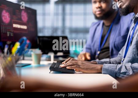 African american server farm worker trying to protect hardware from hacker attack stealing info. Man in data center workplace trying to get rid of virus after seeing security breach alert on display Stock Photo