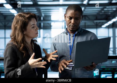 Computer scientists using laptop in data center, managing server virtualization. Teamworking server room colleagues finetuning network protocols, enforcing advanced security measures Stock Photo