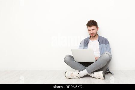Young man working on laptop sitting on floor Stock Photo