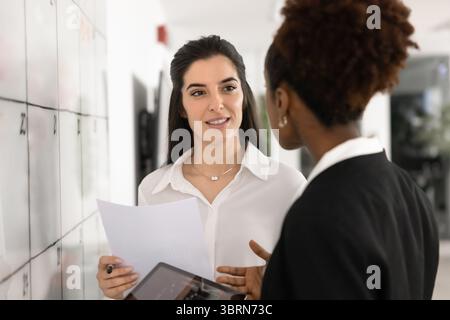 Two professional women reviewing documents, discussing information displayed on tablet Stock Photo