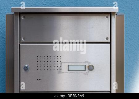 Close-up of a stainless steel intercom system against a blue textured wall, showcasing details like speaker holes, a display, and a button. Stock Photo