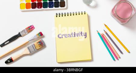 Artistic flat lay of open notebook with creativity word , composition of art tools, brushes, paints around, creative banner Stock Photo