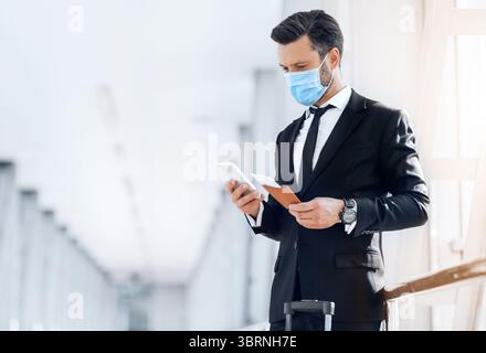 Entrepreneur in face mask using phone while waiting for flight Stock Photo