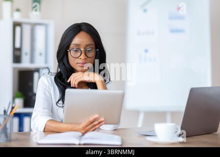 Focused young black business lady using tablet pc at her workplace in modern office, copy space Stock Photo