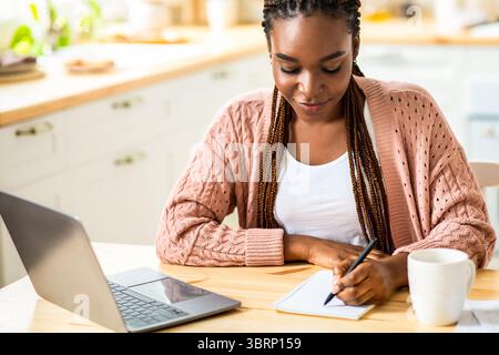 Study At Home. Young Black Female Student Using Laptop In Kitchen Stock Photo