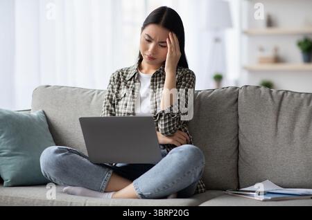 Exhausted korean lady suffering from headache while using laptop Stock Photo