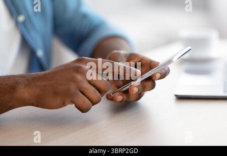Cropped Image Of Unrecognizable Black Man Using Smartphone While Sitting At Desk Stock Photo