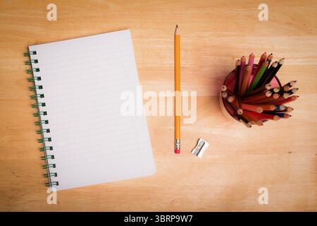 Flat top-down design showing blank spiral notebook on desk with pencil and sharpener, color pencils Stock Photo