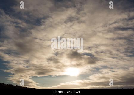 Sunlight is breaking through layered cloud formations in flat design, showing dark ridge silhouette Stock Photo