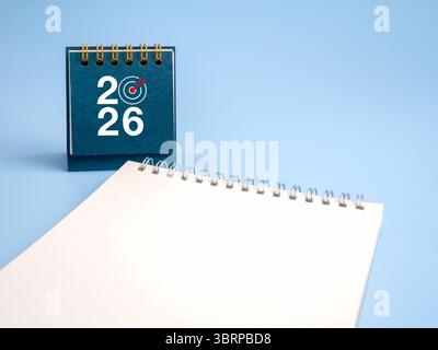 Happy new year 2026. 2026 numbers with target dart icon on blue desk calendar cover, standing near white blank notepad, empty space note page for memo Stock Photo