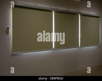 Closed roller blinds, three white curtain or white blinds Roller, sun protection in the dark room, office or meeting room background with nobody. Stock Photo