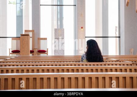 young woman sitting on a church bench facing the Altar Stock Photo