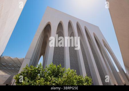 A modern architectural structure with tall arches, under a bright blue sky, with green foliage in the foreground. Stock Photo