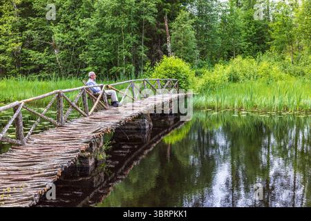 Old man sitting on a bench at a footbridge by a lake Stock Photo