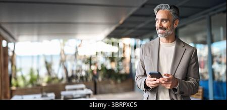 Happy mature business man using phone outdoors. Copy space for ads. Stock Photo