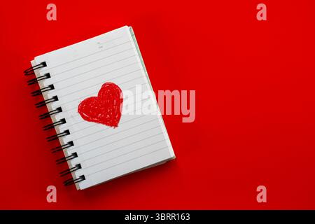 red heart on diary page on red background, crayon sketch of red heart on white notebook paper, Cute valentine's day poster background Stock Photo