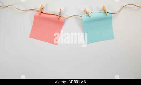Cure pastel blue and pink post-it notes hanging on string, on white background, Boy or Girl - baby gender reveal creative poster background, blank pac Stock Photo