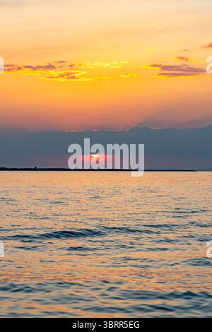 golden sunset on lake Constance, with small waves and illuminated little clouds, sun star reflected in water surface, orange and yellow dominant Stock Photo