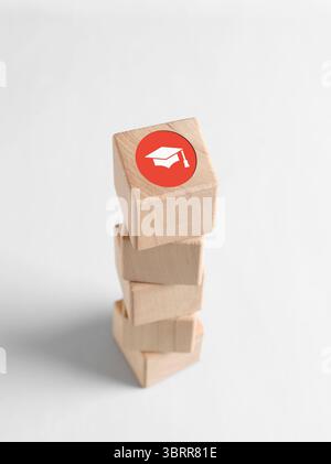 Stacked wooden cubes with a graduation cap icon on top, symbolizing academic success and the pursuit of higher education Stock Photo