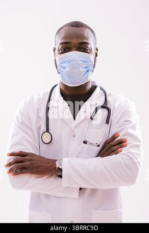 Portrait of confident African American doctor with protective mask in medical uniform standing in front of gray background. Stock Photo