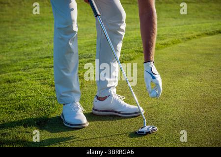 Golf player placing golf ball on the green grass with a club during a sunny day Stock Photo