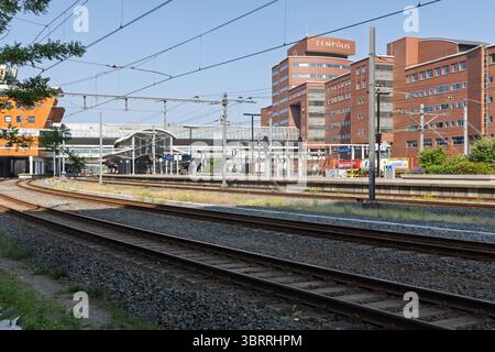 Train tracks leading into a station with modern buildings, including "EEMPOLIS," under a clear blue sky. Amersfoort, Netherlands, 12 June 2025. Stock Photo