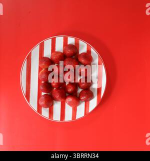 Red ripe strawberries on red striped plate with red background Stock Photo