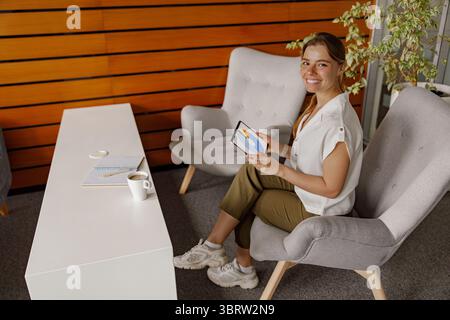 A modern workspace featuring a young woman comfortably using her tablet in a cozy setting Stock Photo