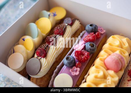 Delicious eclairs with fresh berries and macarons beautifully displayed in a bakery box. A close-up of colorful eclairs, adorned with fresh berries, a Stock Photo