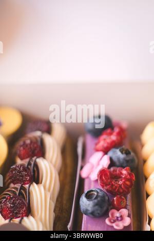 Delicious eclairs with fresh berries and macarons beautifully displayed in a bakery box. A close-up of colorful eclairs, adorned with fresh berries, a Stock Photo