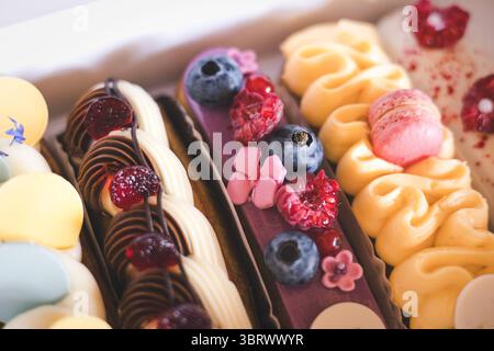 Delicious eclairs with fresh berries and macarons beautifully displayed in a bakery box. A close-up of colorful eclairs, adorned with fresh berries, a Stock Photo