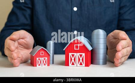 A man protects a large and small farm with his hands. Protection of farms. Support for all-scale agriculture. Equitable policy, resilience against glo Stock Photo