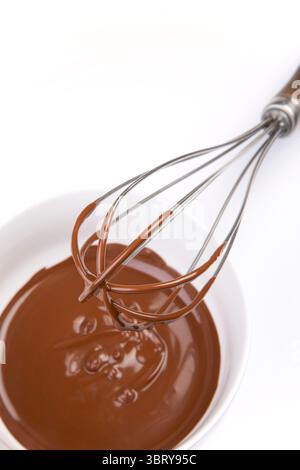 confectioner whisking melted chocolate in porcelain bowl holding whisk above view Stock Photo