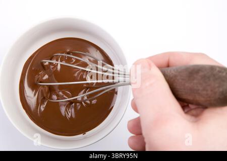 confectioner whisking melted chocolate in porcelain bowl holding whisk above view Stock Photo