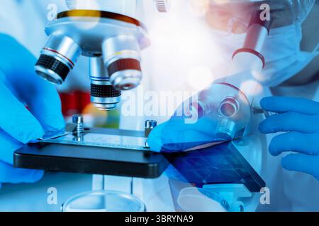 Close up scientist hands with gloves adjusting glass slide under microscope in laboratory with blue light. Concept of scientific research, medical tes Stock Photo