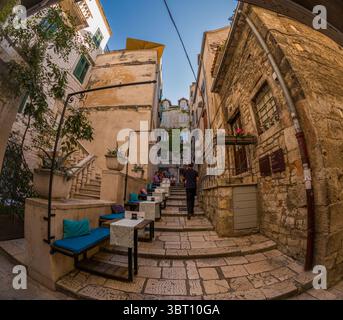 Split, Croatia - September 8th 2023: A person walks up stone steps past an outdoor cafe in Split. The cafe is built into the steps, offering a unique Stock Photo