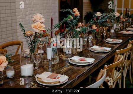A beautifully set wedding table features elegant floral centerpieces with roses and eucalyptus, complemented by candles and stylish dinnerware on a ru Stock Photo
