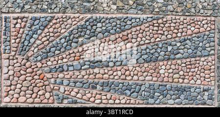 Close-up of decorative pebble outdoor mosaic with radiating pattern as image of sun made from natural stones in various colors and textures, embedded Stock Photo