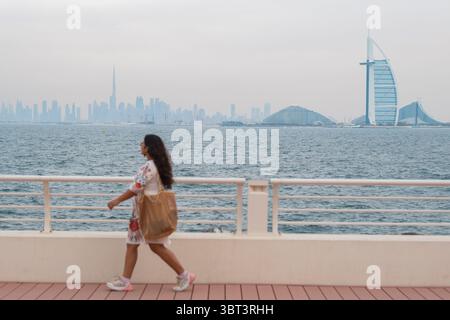 Woman traveler enjoying seaside walk with dubai skyline landmarks, with burj khalifa and burj al arab in background Stock Photo