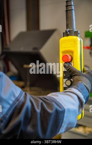 Factory worker wearing gloves using a control pendant, pushing red emergency button on yellow control panel Stock Photo