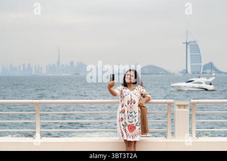 Dubai promenade walk with woman tourist taking photos and skyline in background Stock Photo