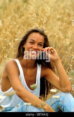 auburn hairyoung pretty woman smiling front camera sit down in a straw field spring time Stock Photo