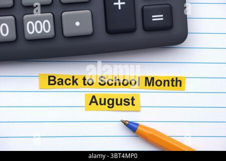 Yellow strips of paper with the words Back to School Month - August typed on them lying in an open notebook near a calculator and ballpoint pen. Close Stock Photo