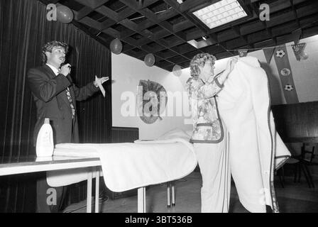 Health the choice IJm. IJmuiden The Netherlands, Whizgle News, Dutch Desk, The Netherlands, 1950 - 2000 on 21-06-1994. These are the elements in the image. In a setting that appears to be an indoor event space, there are two individuals engaged in a presentation. One person, dressed in a formal dark suit with a patterned tie, stands at a table, animatedly gesturing with one hand while holding a microphone in the other. This individual has curly hair and exudes an energetic, engaging presence. The second person is slightly turned away from the viewer, showcasing a light-colored outfit with flor Stock Photo