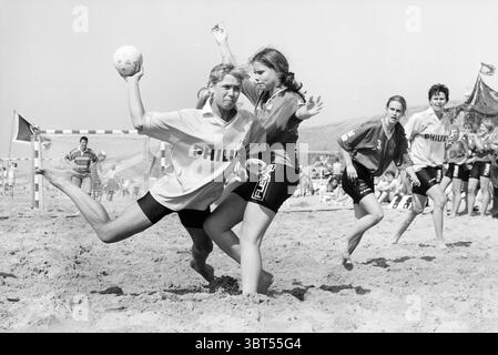 Beach handball OSC-PSV Bloemendaal Bloemendaal, Whizgle News, Dutch Desk, The Netherlands, 1950 - 2000 on 01-06-1996. The image contains these topics. The scene captures an energetic beach handball match, set against a bright, sunlit backdrop. The sandy beach stretches far in the foreground, dotted with players and a few scattered beachgoers in the background. Central to the action are two athletes engaged in a dynamic play. One player, mid-throw, is airborne with one leg extended behind, showcasing agility and determination. Dressed in a light-colored jersey, the fabric billows slightly, indi Stock Photo